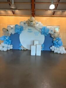 Blue and beige balloon arch with “Baby Aulakh” message and white floral accents by Iconic Events Edmonton. Making Every Event in Edmonton Iconic.