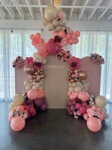 Elegant floral and balloon display in shades of blush, peach, and burgundy for EMBRAACED event by Iconic Events Edmonton. Making Every Event in Edmonton Iconic.