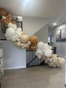 Neutral-toned balloon garland on staircase with white floral accents by Iconic Events Edmonton. Making Every Event in Edmonton Iconic.